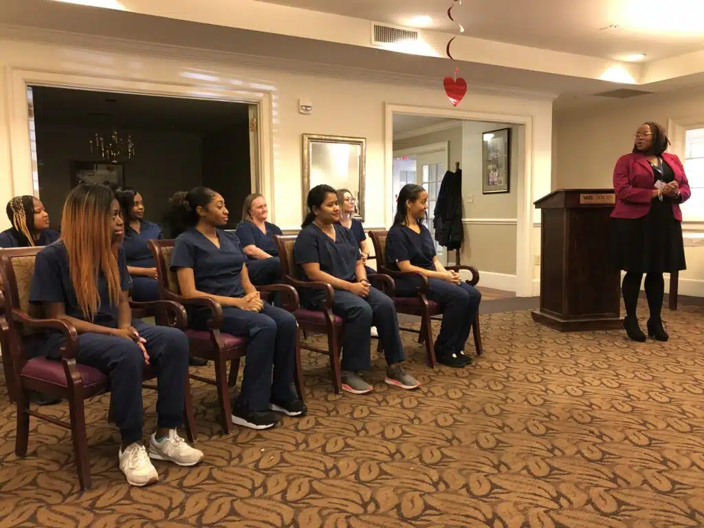 Virginia Health Services graduates group photo in The Arbors dining room. The eight students are pictured with instructor Princess Henderson.