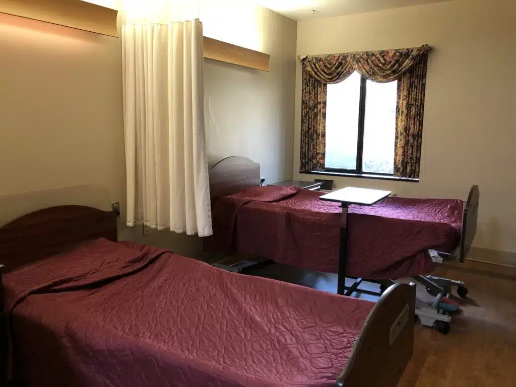 Double rooms on the expanded Memory Care unit have two beds separated by a curtain and a window for natural light covered by a window treatment.