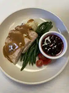 Plated sliced turkey with gravy, mashed potatoes, green beans and cranberry sauce.