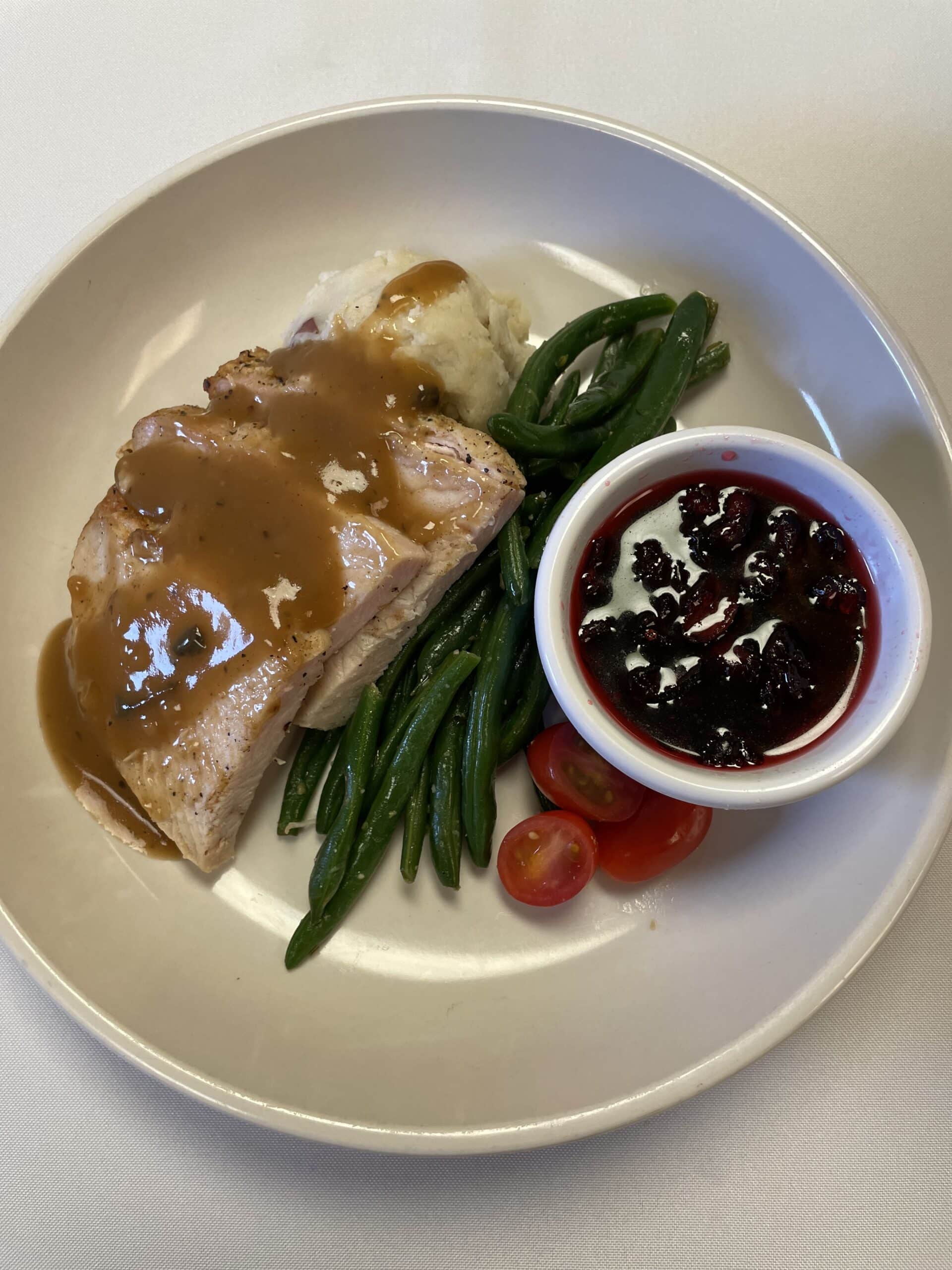 Plated sliced turkey with gravy, mashed potatoes, green beans and cranberry sauce.