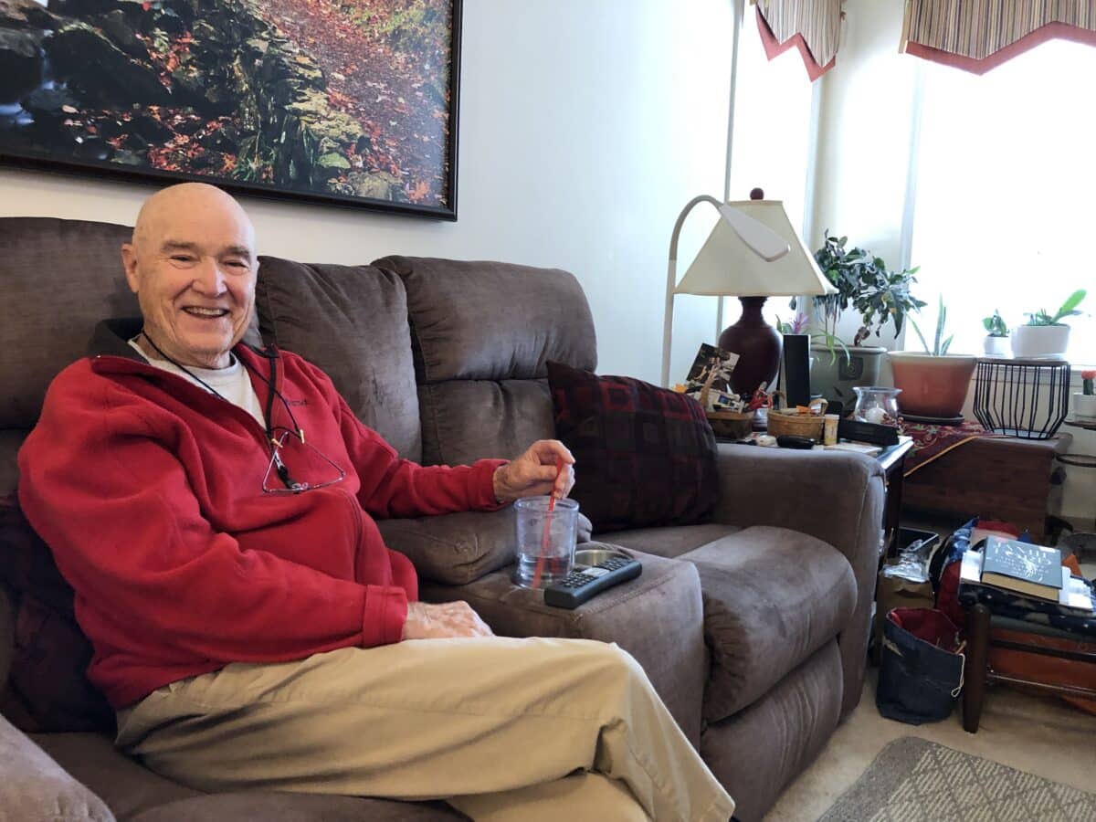 Maynard Sandford sits on the couch in his Arbors apartment, smiling.