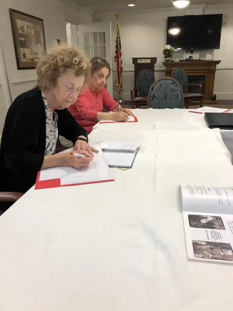 Faye sits and writes at a table, with another resident beside her.