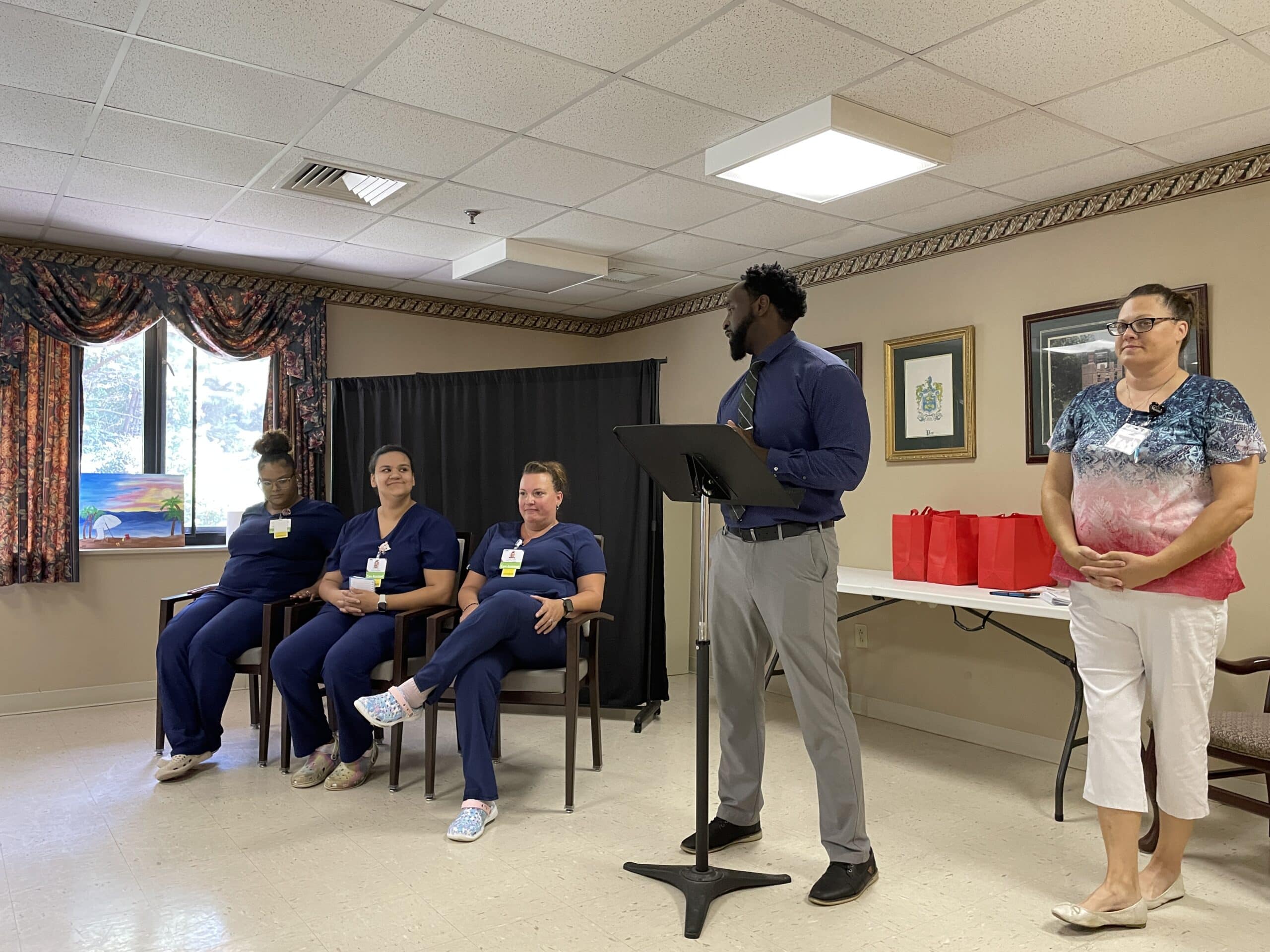 Walter Reed Administrator Bryant Hudgins addresses the three graduates from the podium as instructor Tracy Williams looks on.